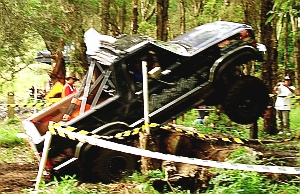 1986 Ford Bronco - An off-road vehicle is overturned in a forest setting, with onlookers present.