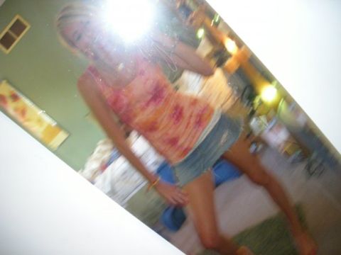 1989 Ford Bronco - A woman captures a mirror selfie while wearing a tie-dye top and denim shorts, with a reflection showing a room interior.