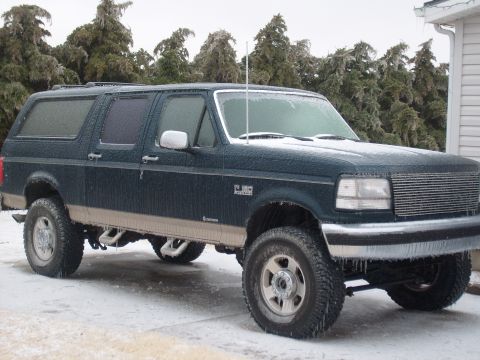 1995 Ford C-350 (Centurion Conversions) - A dark green SUV with tan trim is covered in ice, parked on a snowy surface with icy trees in the background.