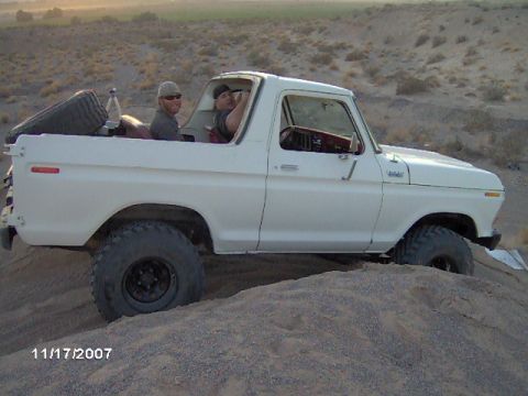 1979 Ford Bronco - White Ford Bronco with two occupants navigates a sandy incline, spare tire visible in the cargo area.