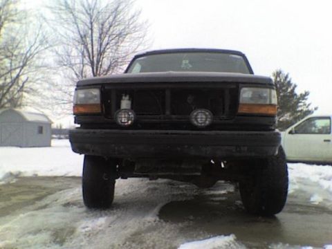 1995 Ford Bronco - Front view of a black Ford Bronco parked in a snowy area with a shed and another vehicle in the background.