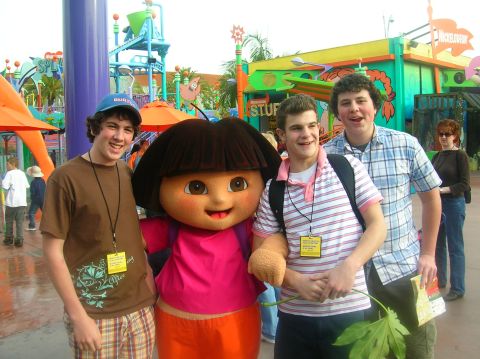 1996 Ford Bronco - Three young men pose with the Dora the Explorer mascot at an amusement park, with colorful attractions in the background.