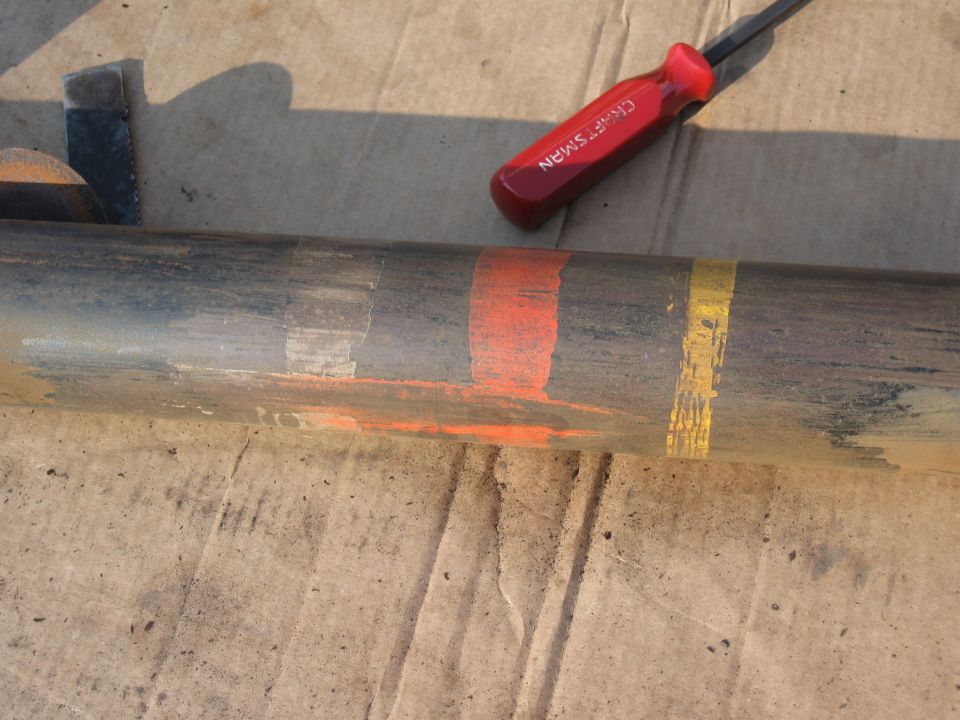 Suspension component with orange, white, and yellow paint marks. Screwdriver with red handle is visible