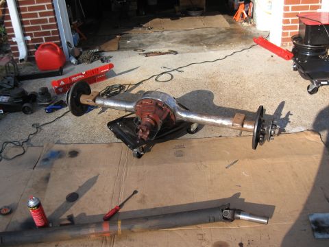 1968 Shelby GT500 - A rear axle assembly and driveshaft are laid out on cardboard in a garage, surrounded by tools and car parts.