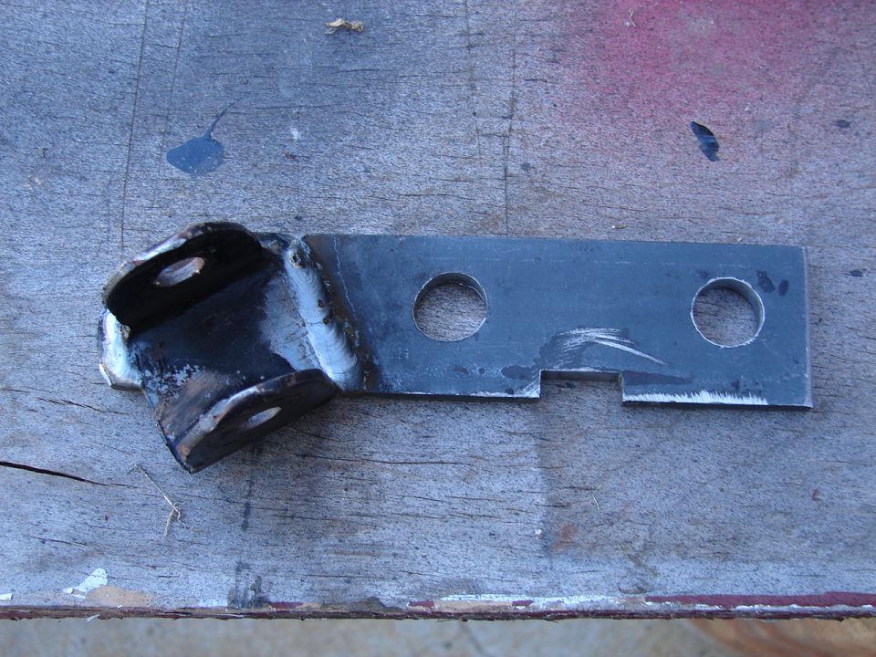 Custom welded steel bracket with drilled holes and notched end on a plywood workbench