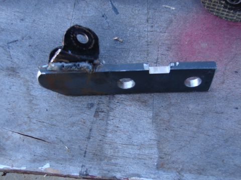1973 Ford Ranchero - A black-painted steel mounting bracket with a welded tab featuring a single pivot hole, plus two drilled holes along the flat bar. It rests…