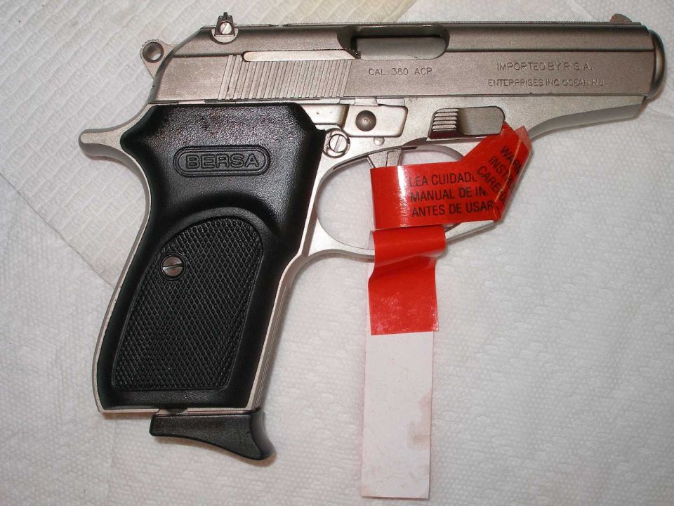 Nickel Bersa .380 ACP pistol with black grips and red safety warning tag on white cloth