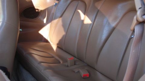 1996 Ford Probe - The interior of a car shows tan leather seats and seat belts, with a speaker grille visible on the side.