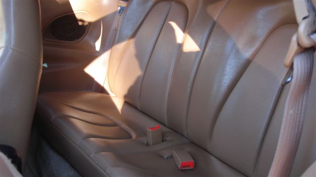 Tan leather rear seat and seatbelt buckles inside a coupe, sunlit