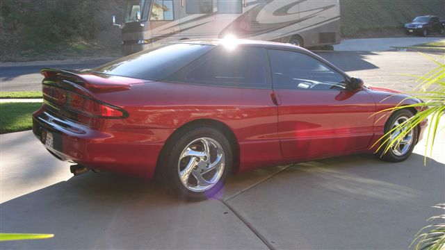 Red 1996 Ford Probe parked on driveway, side view. RV and another car in background