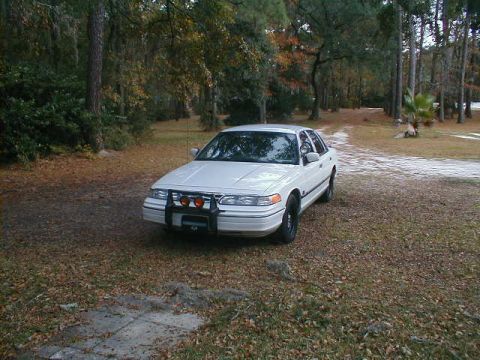 1994 Ford Crown Victoria - This 1994 Ford Crown Victoria is seen from a three-quarter front view, parked in a wooded area with a push bar and auxiliary lights.