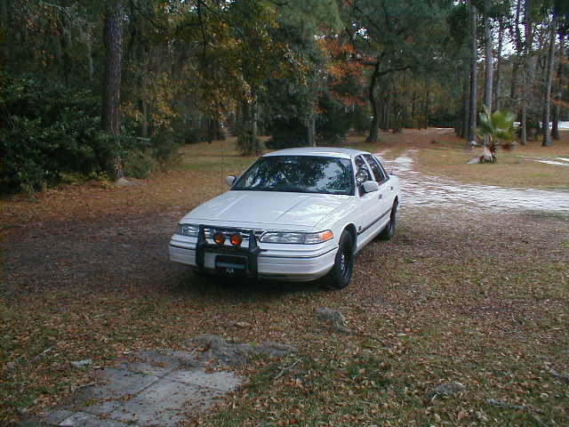 White 1994 Ford Crown Victoria with push bar and auxiliary lights, parked outdoors