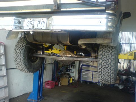 1985 Ford Bronco - Vehicle's rear axle and suspension are visible while it's raised on a lift in a garage.
