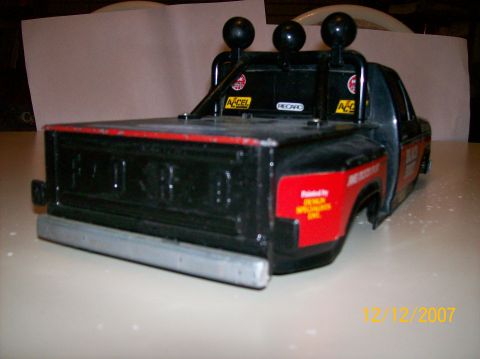 1979 Ford Bronco - Rear three-quarter view of a black and red scale-model Ford pickup on a tabletop, showing the embossed FORD tailgate, chrome rear bumper an…