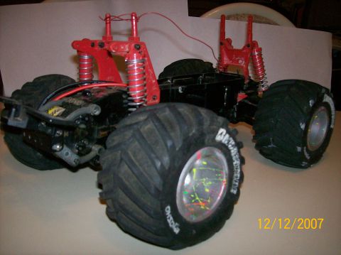 1979 Ford Bronco - A bodyless RC monster truck chassis on a tabletop, showing a black plastic frame with red shock towers, chrome-bodied coil-over shocks and…