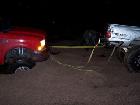 1991 Ford Bronco - Two trucks are stuck in the sand at night, with one attempting to tow the other.