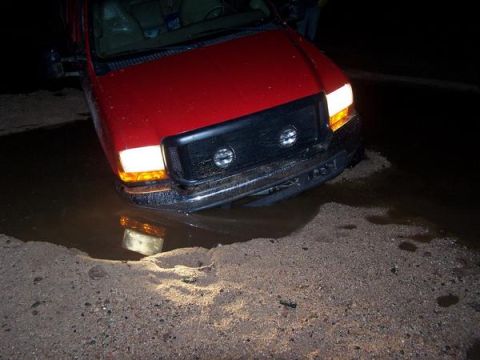 1991 Ford Bronco - A red SUV is stuck in a large puddle of water, its front end submerged.