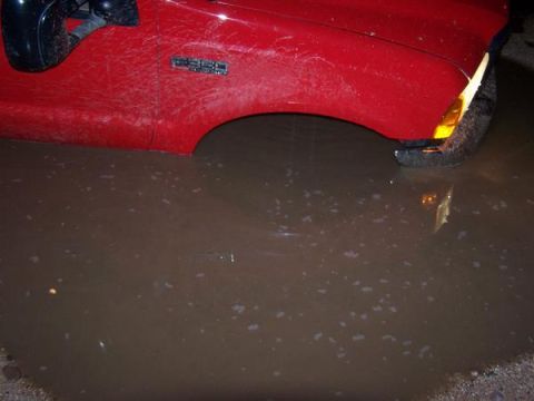 1991 Ford Bronco - A red truck's front fender and tire are partially submerged in a large puddle of muddy water.