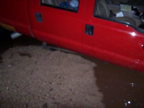 1991 Ford Bronco - Red pickup truck driving through shallow water, showing its side profile and interior.