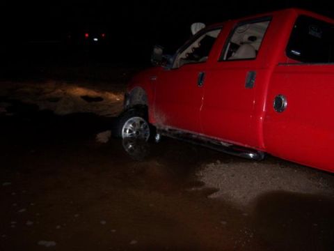 1991 Ford Bronco - A red pickup truck is partially submerged in water at night, with its front wheel deep in the murky liquid.