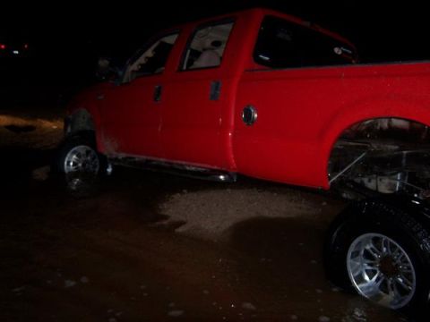 1991 Ford Bronco - A red pickup truck is shown from the side at night, with its lifted suspension and chrome wheels visible.