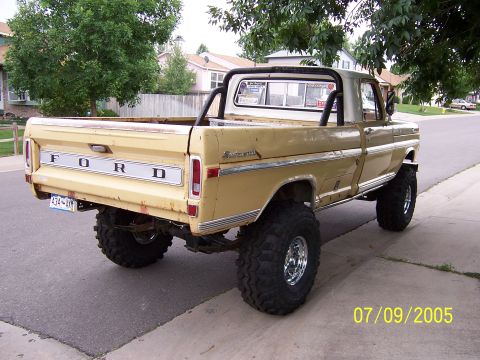 1994 Ford Bronco - This lifted yellow Ford pickup truck, seen from the rear, features large off-road tires and the iconic 'FORD' tailgate.