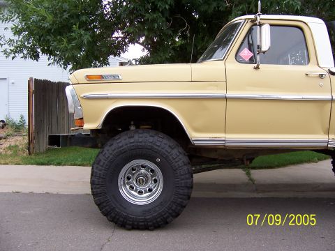 1994 Ford Bronco - Side view of a lifted, yellow 1970s Ford F-Series truck with prominent chrome trim and large off-road tires.