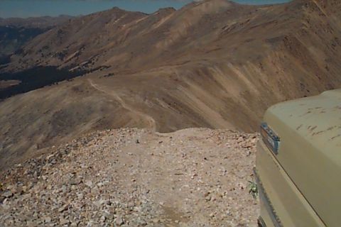 1994 Ford Bronco - Mountain landscape with a dirt road and the corner of a tan vehicle visible on the right.