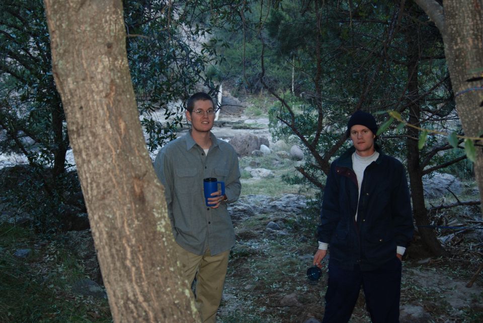 Two men in a wooded area, one holding a blue cup