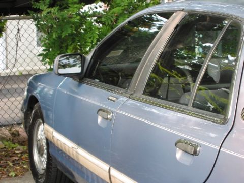 1993 Mercury Grand Marquis - The side profile of a blue sedan shows its doors, windows, and side mirror.