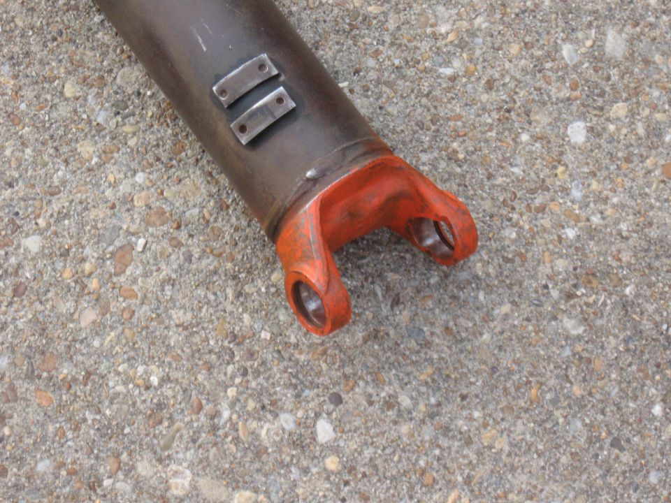 Driveshaft yoke with orange painted ends and two metal plates welded to the dark shaft