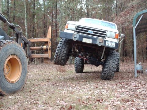1990 Ford F-150 - Ford F-150 lifted by a front loader, showing its large tires and modified suspension.