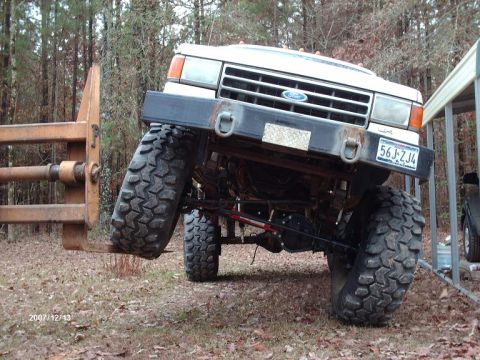 1990 Ford F-150 - White Ford truck with a modified suspension and large tires is shown from the front.
