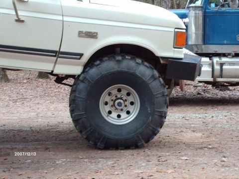 1990 Ford F-150 - A white Ford F-150 is shown with large off-road tires, parked next to a blue semi-truck.