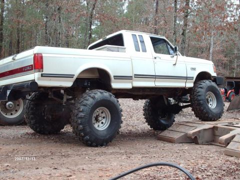 1990 Ford F-150 - White 1990 Ford F-150 pickup truck modified with a lift kit and large off-road tires.
