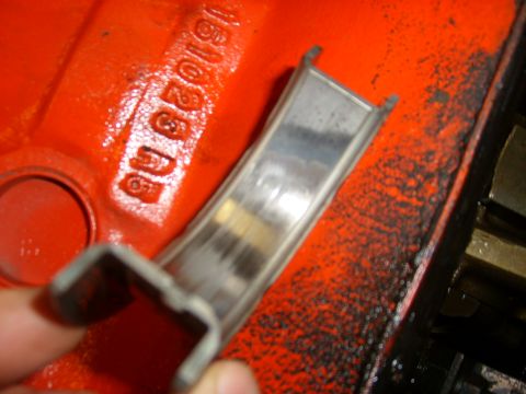 1994 Ford Bronco - A hand holds a metal bearing part above an orange engine block with stamped numbers visible.