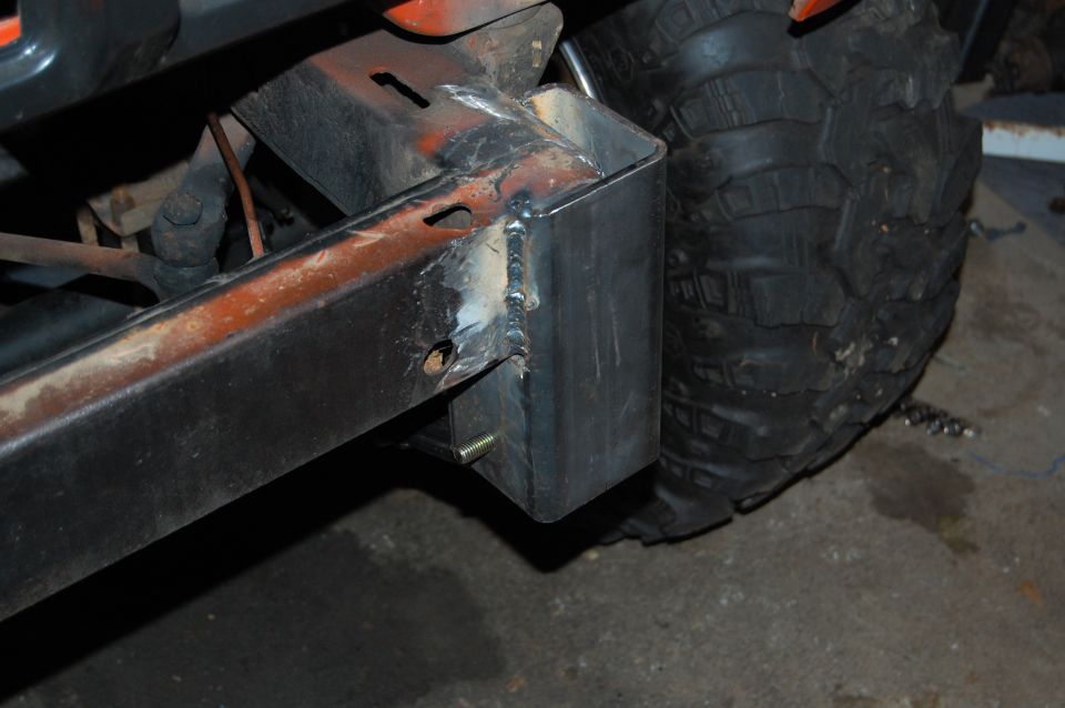 Custom metal bumper mount with welds, next to a large off-road tire. Orange paint visible on frame
