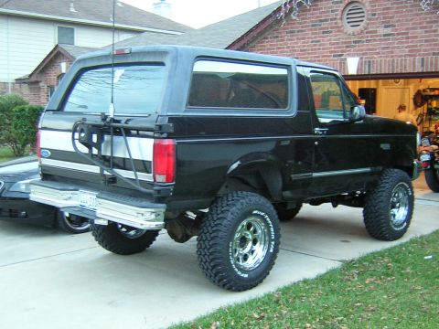 1994 Ford Bronco - Rear view of a black Ford Bronco with a spare tire mounted on the back, showing its lifted stance and custom wheels.