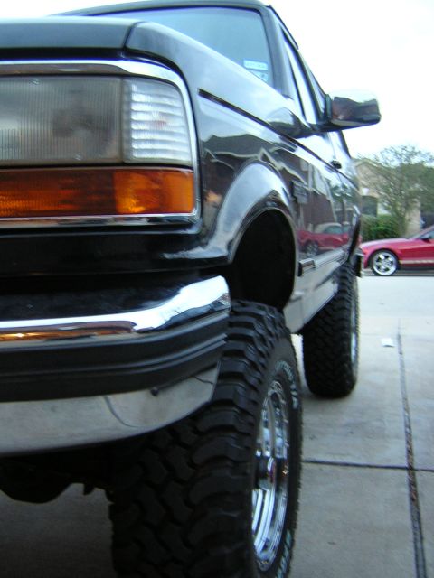 1994 Ford Bronco - This lifted 1994 Ford Bronco features large off-road tires and chrome wheels, seen from a low-angle front three-quarter view.