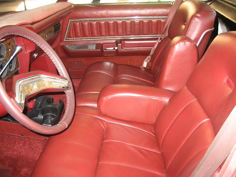 1979 Ford Ranchero - The interior of a vehicle features red leather seats and door panels, with a view of the steering wheel and dashboard.