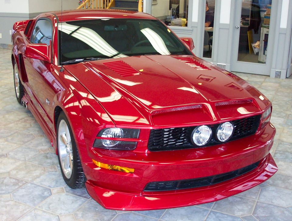 Red Ford Mustang parked indoors, front quarter view. Watermark says SUPERMOTORS.NET