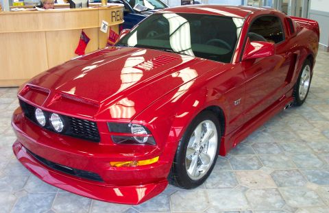 2008 Ford Mustang - Red Ford Mustang GT with custom body kit and wheels, seen from the front three-quarter angle.