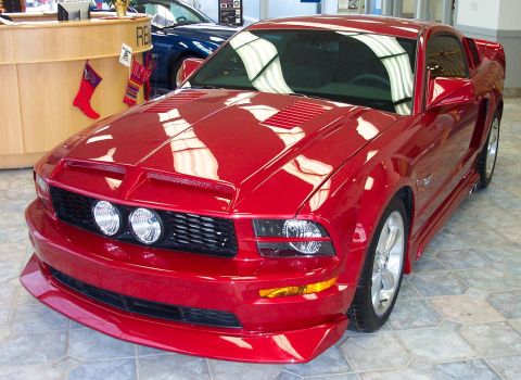 2008 Ford Mustang - Red 2005 Ford Mustang with a custom hood scoop and front bumper is parked indoors, with another blue vehicle visible in the background.