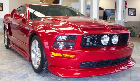 2008 Ford Mustang - This red sports coupe features a distinctive grille and aggressive body kit, parked on a tiled floor inside a building.