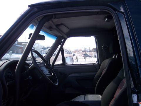 1995 Ford Bronco - The interior of a dark SUV with a roll cage is visible from the driver's side.