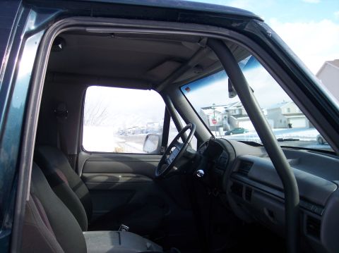 1995 Ford Bronco - The interior of a 1995 Ford Bronco, a roll cage and grey upholstery, is visible through the driver's side door.