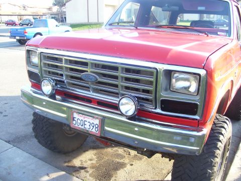 1986 Ford Bronco - Front view of a red 1986 Ford Bronco, its chrome grille, auxiliary lights, and a California license plate.