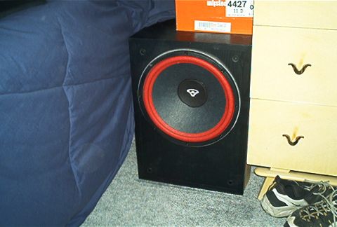 1985 Ford LTD Crown Victoria - A black subwoofer speaker with a red surround is placed on a carpeted floor next to a wooden dresser.