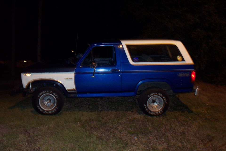 Side view of a blue and white Ford Bronco parked on grass at night