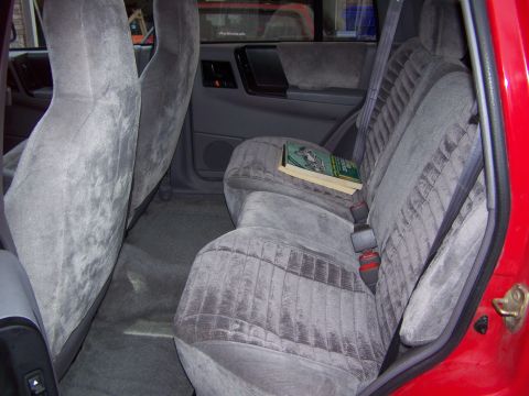 1994 Jeep Grand Cherokee - The interior of a red Jeep Grand Cherokee shows grey velour seats and a book on the rear bench.